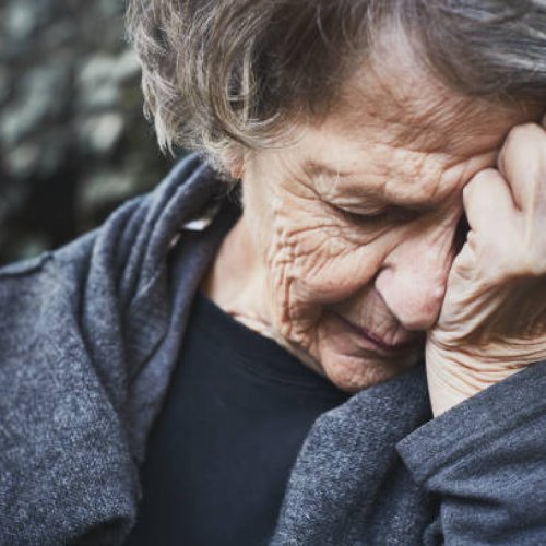An old woman looks miserable and exhausted, he head in her hands.